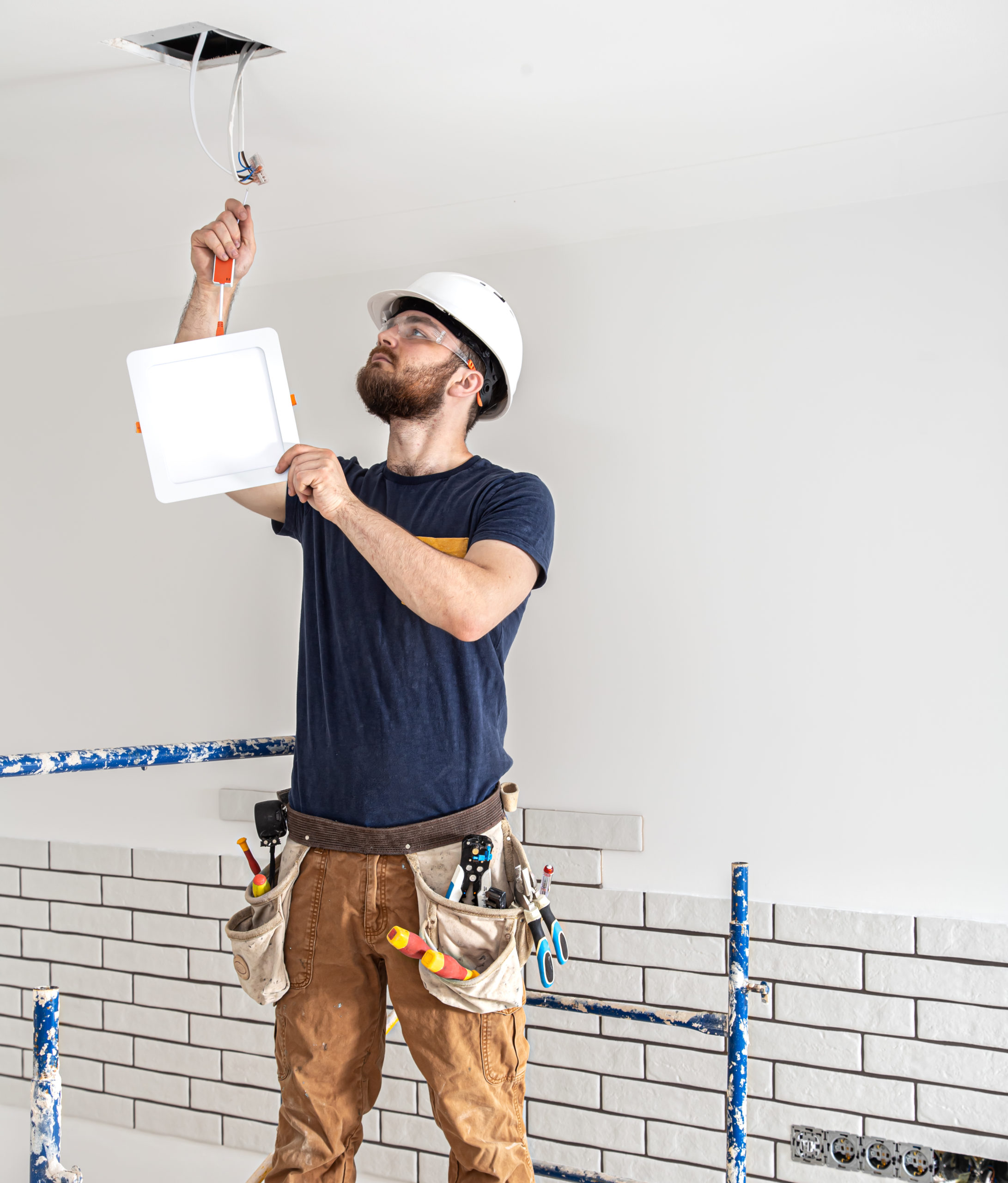 Electrician builder worker in a white helmet, installation of lamps at height copy space.
